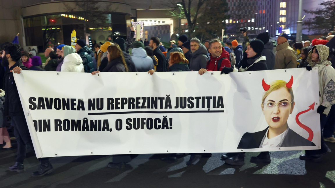 Демонстранти носят огромен транспарант по време на протест за независимост на съдебната система в центъра на Букурещ, на 14 декември 2025 г. Поредицата протести, организирани от 6 неправителствени организации, започнаха след излизането на документалния филм "Правосъдие в плен". На транспаранта пише "Савоня не представлява  правосъдието, а просто го души!", визирайки Лия Савоня, председател на Висшия касационен съд.