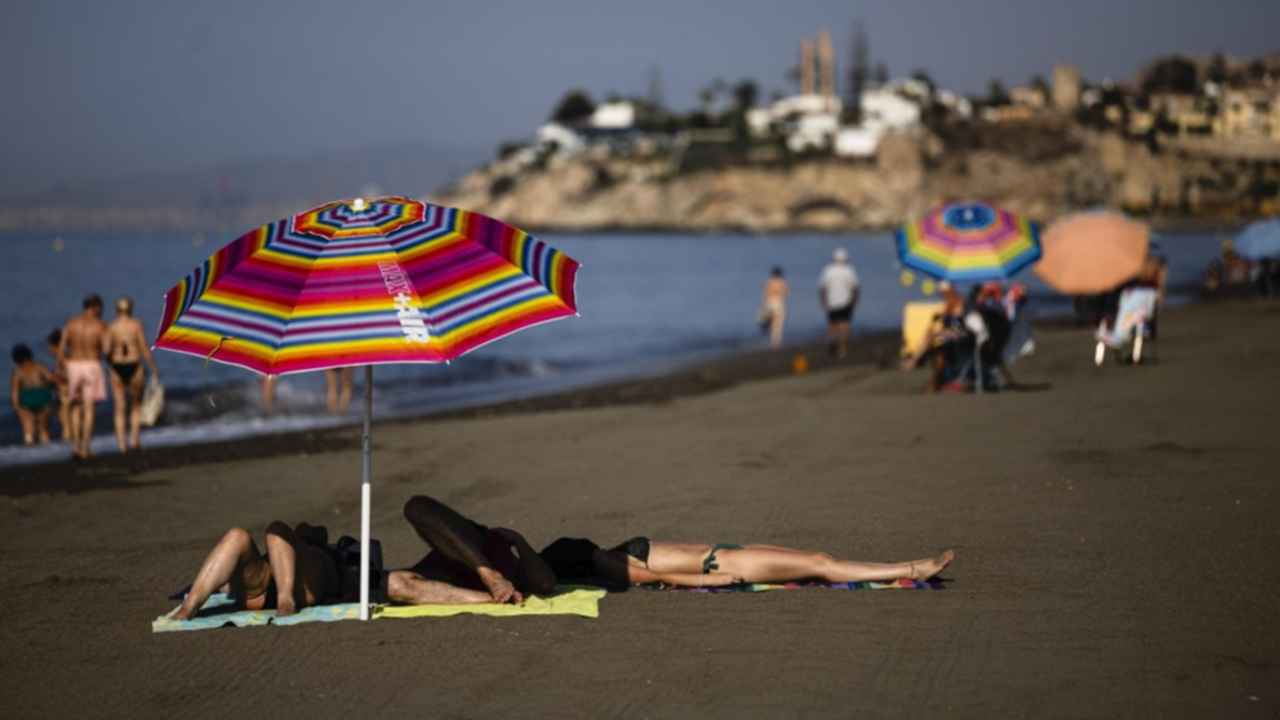 Хора релаксират под чадър на плажа Ел Ринкон де ла Виктория в Малага, Испания, 13 август 2025 г.